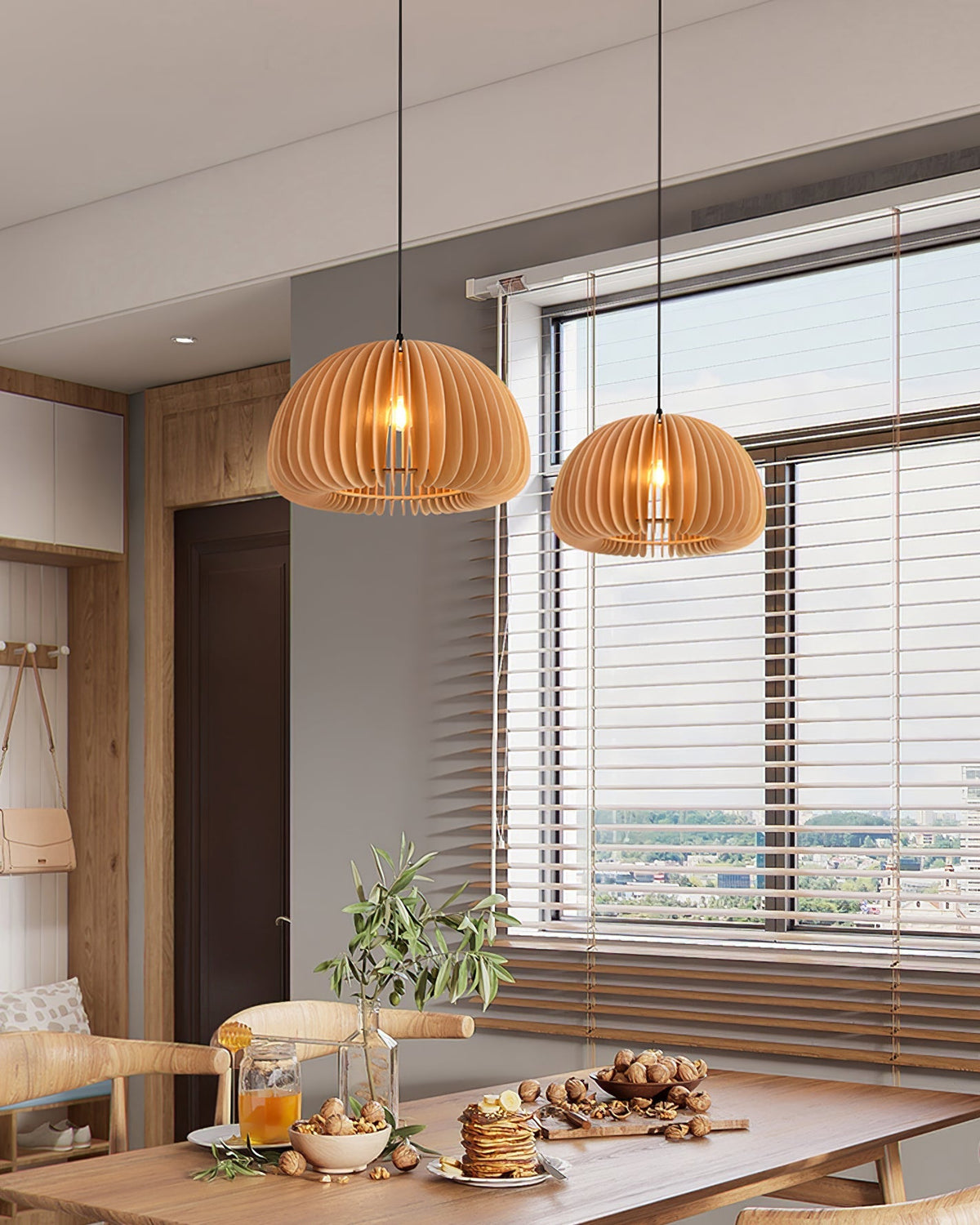 Two Clérachic slatted pendants of different sizes hung in a kitchen-diner, beside a window with horizontal blinds and a laid table.
