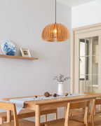 A Clérachic slat pendant over a pale dining table with a vase of dried stems, beside a small shelf with a blue-and-white plate.