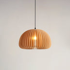 Clérachic wood pendant on a black cord against a pale wall, its slats curving around the lit bulb in a soft, even glow.