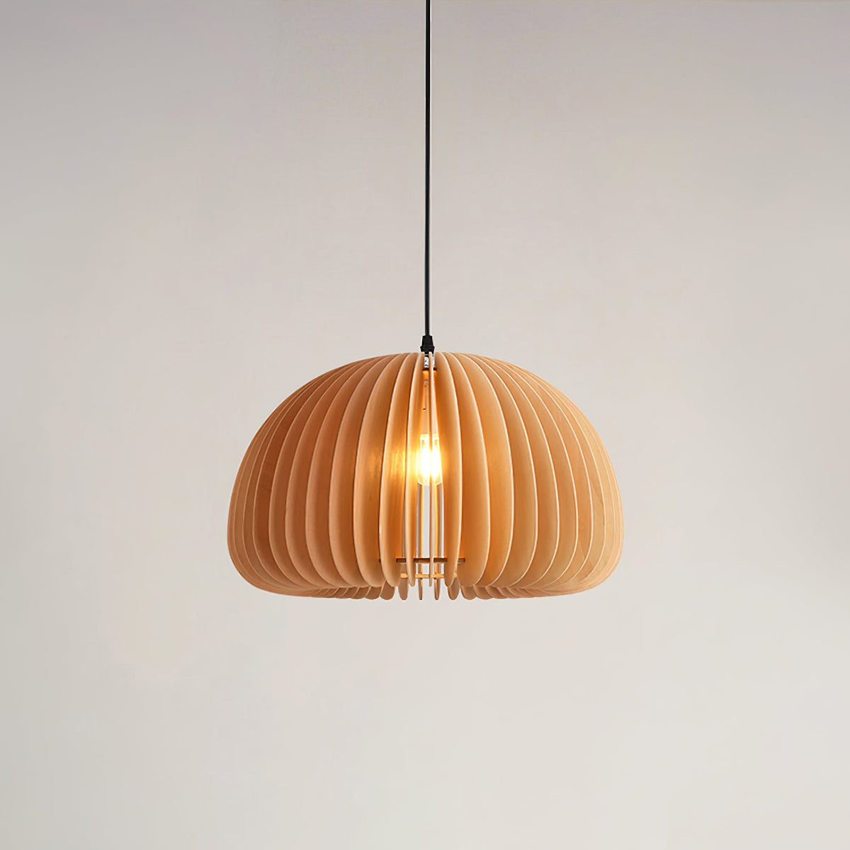 Clérachic wood pendant on a black cord against a pale wall, its slats curving around the lit bulb in a soft, even glow.
