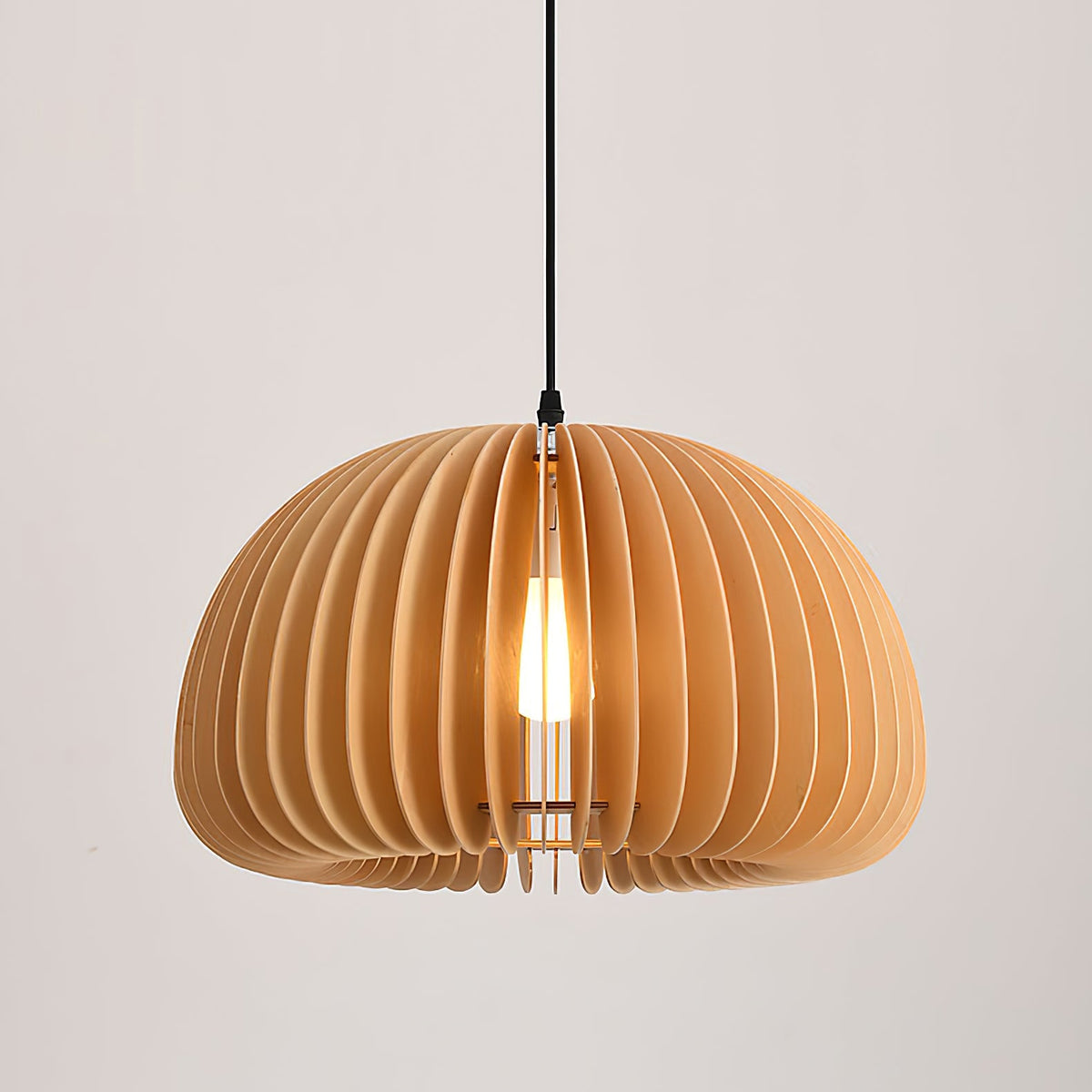Clérachic slat pendant with a bright bulb inside, hung close to a pale wall with a taupe tone and soft light.