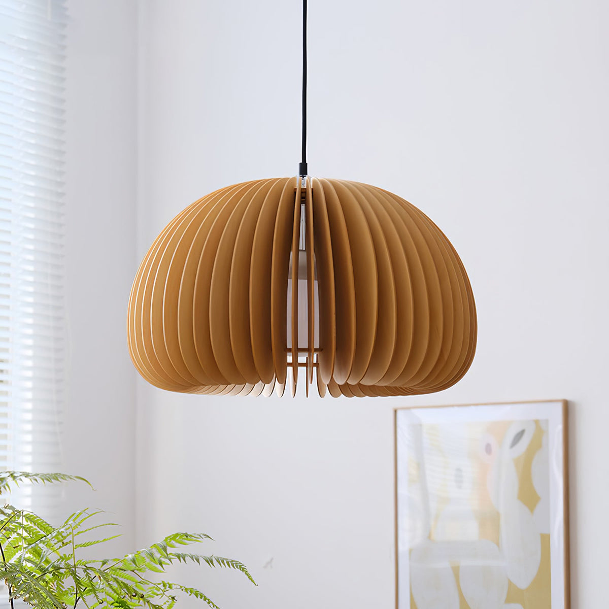 The Clérachic slatted pendant, shown larger and slightly turned, beside a plant and a framed poster on a pale wall.