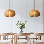 Two Clérachic slat pendants hung over a table with pale wooden chairs, in a white panelled room with a vase of eucalyptus.