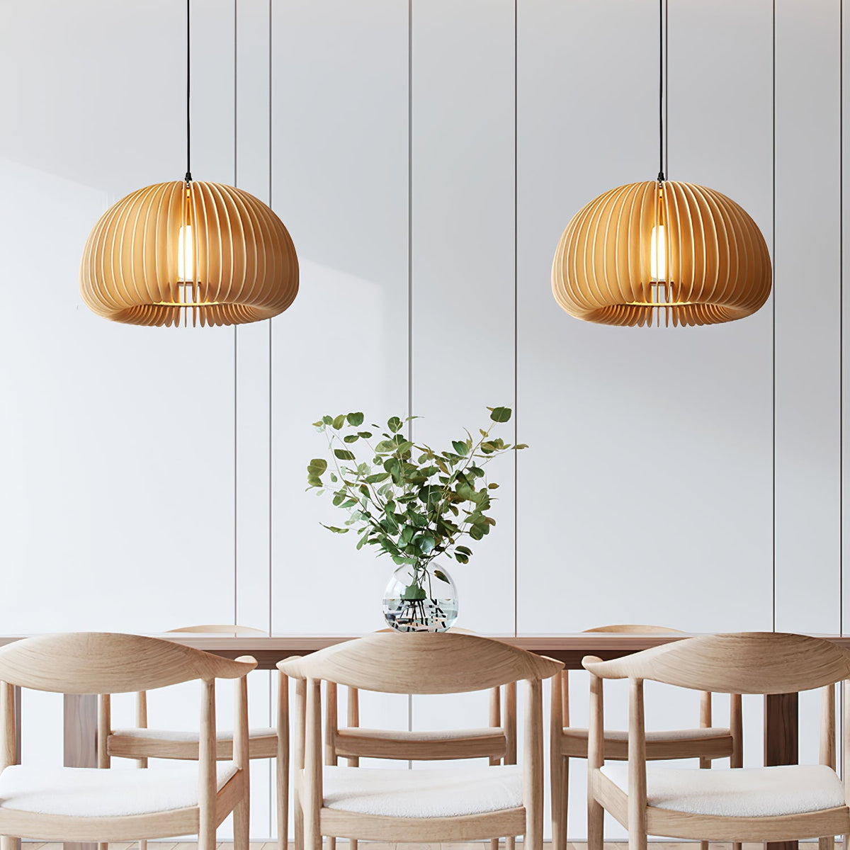 Two Clérachic slat pendants hung over a table with pale wooden chairs, in a white panelled room with a vase of eucalyptus.