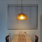 Clérachic wooden pendant lit in front of a grey window blind, above a table with a small framed card and wooden chairs.