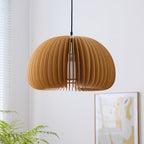 The same Clérachic slatted pendant at a lower angle in front of a pale wall, with a fern and a framed poster in the corner.