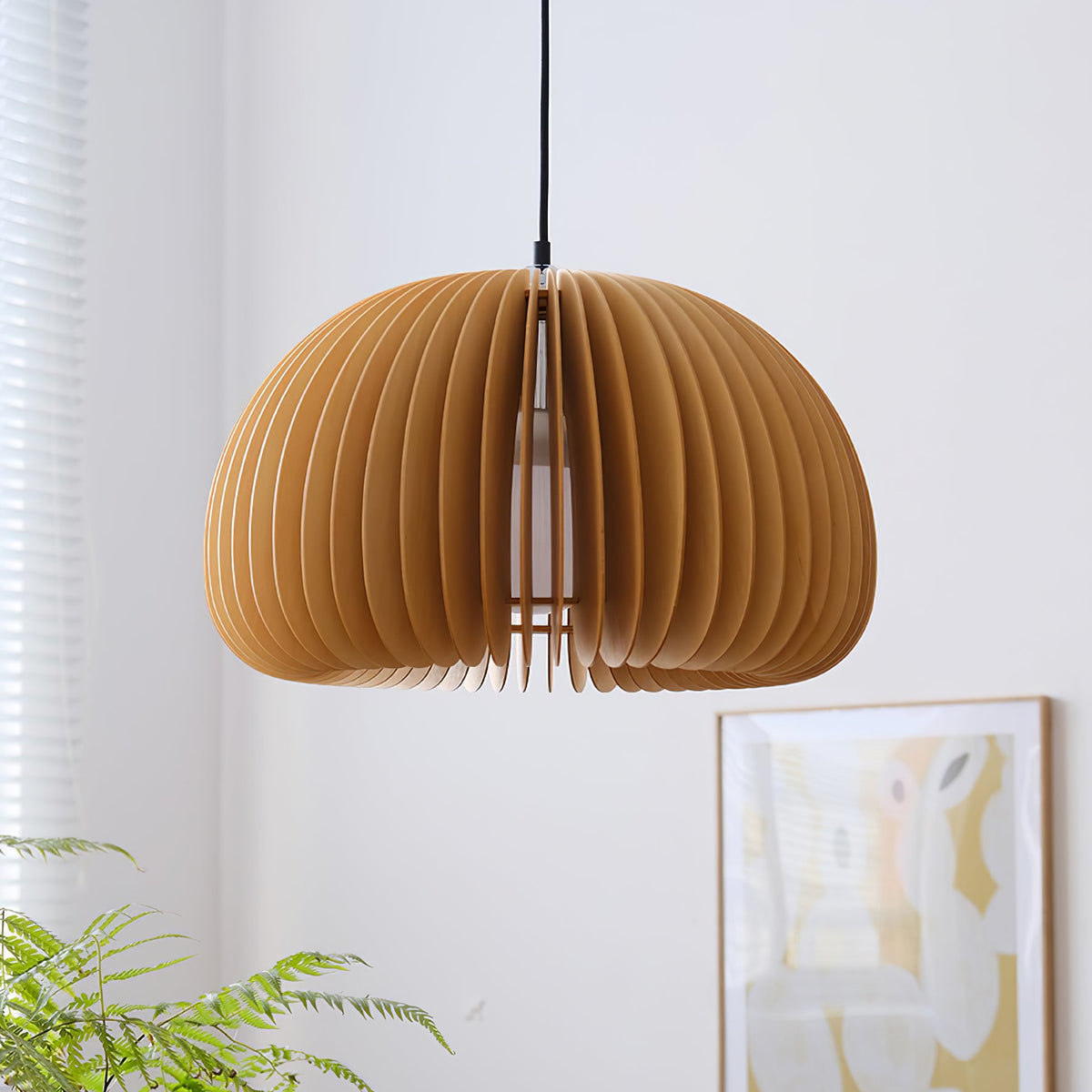 The same Clérachic slatted pendant at a lower angle in front of a pale wall, with a fern and a framed poster in the corner.