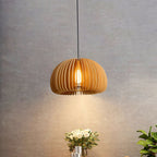 A Clérachic wood slat pendant lit above a bouquet of white roses, in front of a rough grey wall with a warm glow below.