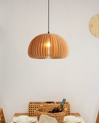 Clérachic slatted pendant hung in front of a pale wall, with a wicker basket, a bottle and plates on a dining table below.