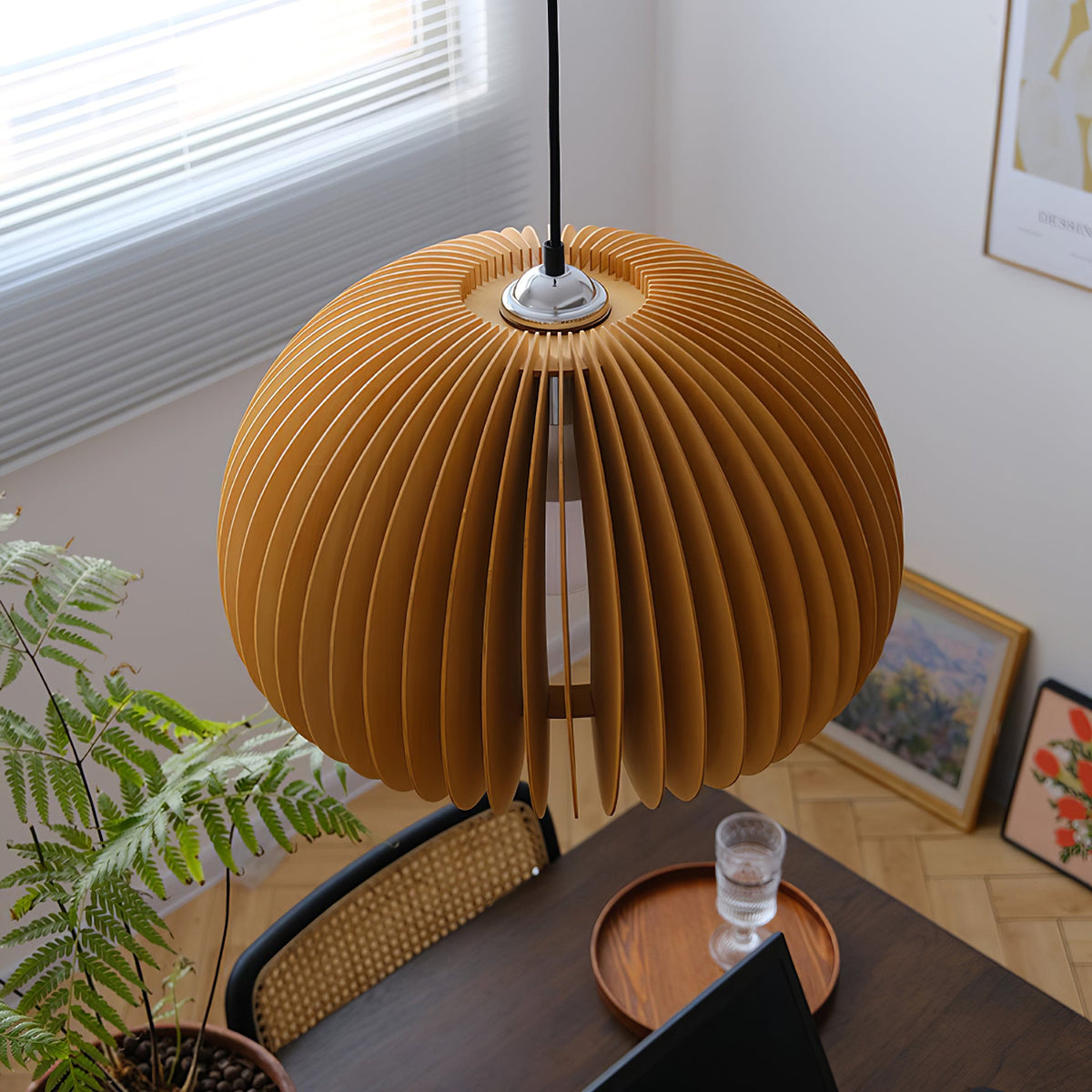 Clérachic slatted pendant seen from above, hanging over a dark table with a wooden tray, a glass and a green fern by a window.