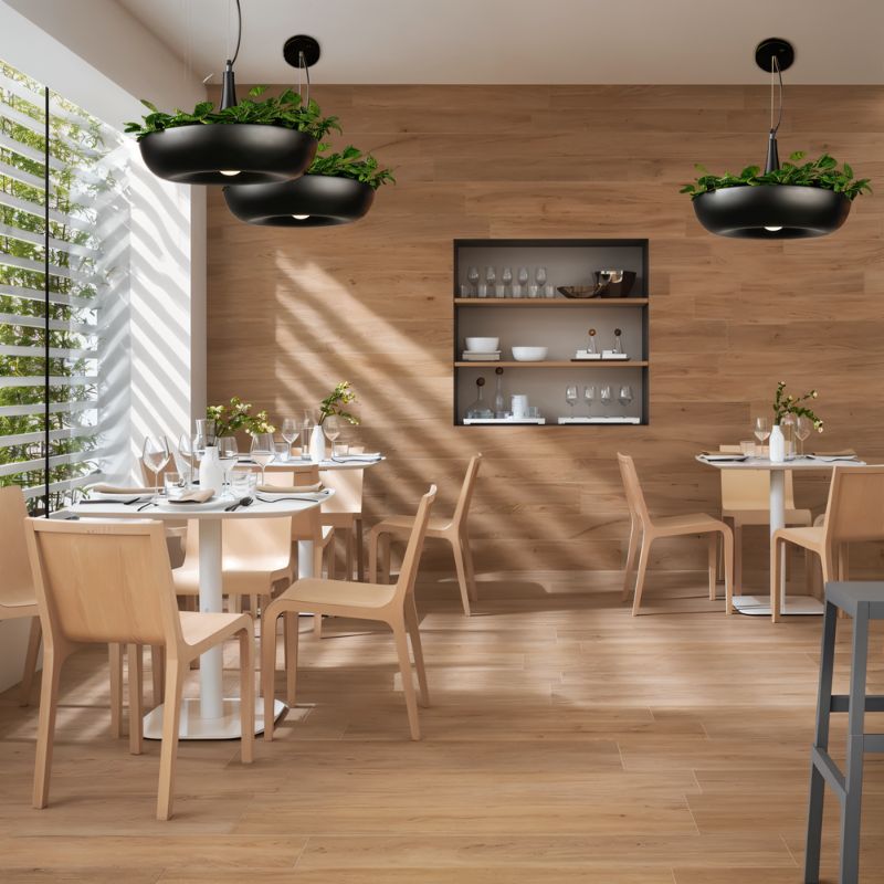 Clérachic black bowl pendants topped with greenery, hung in a bright wood-panelled dining room with round tables and pale chairs.