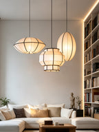 Three ribbed fabric pendants from this Clérachic fixture, in different shapes, cluster above a sofa beside a bookshelf.