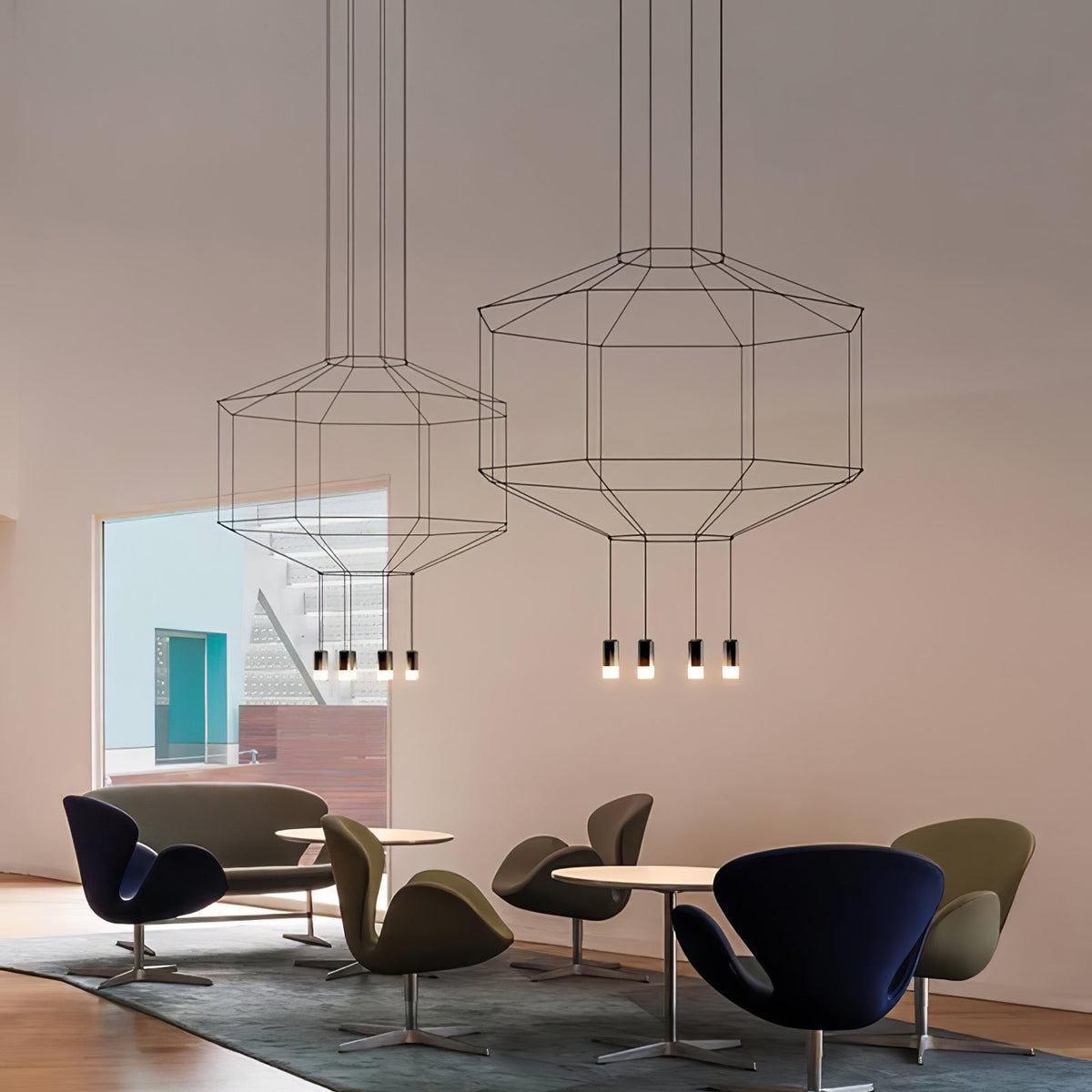 Two Clérachic wireframe pendants with clusters of small lights hang in a lounge with dark swivel armchairs and round tables.