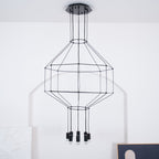 Unlit black cable-frame pendant with a tiered cage and a cluster of dark light heads, on a white wall, from Clérachic.