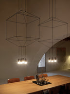 Close framing of two cable-frame pendants glowing above an oak table with a glass tray, from Clérachic.