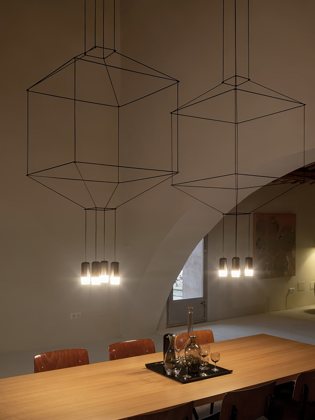 Close framing of two cable-frame pendants glowing above an oak table with a glass tray, from Clérachic.