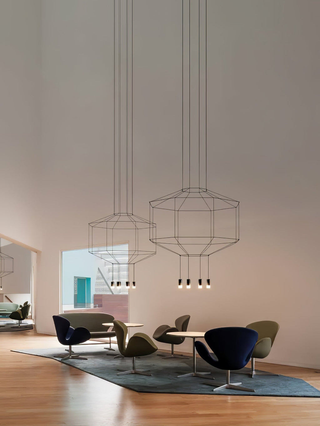 Two Clérachic wireframe pendants hang high in a tall room above a seating group of olive and navy armchairs.