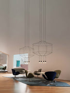 Two Clérachic wireframe pendants hang high in a tall room above a seating group of olive and navy armchairs.