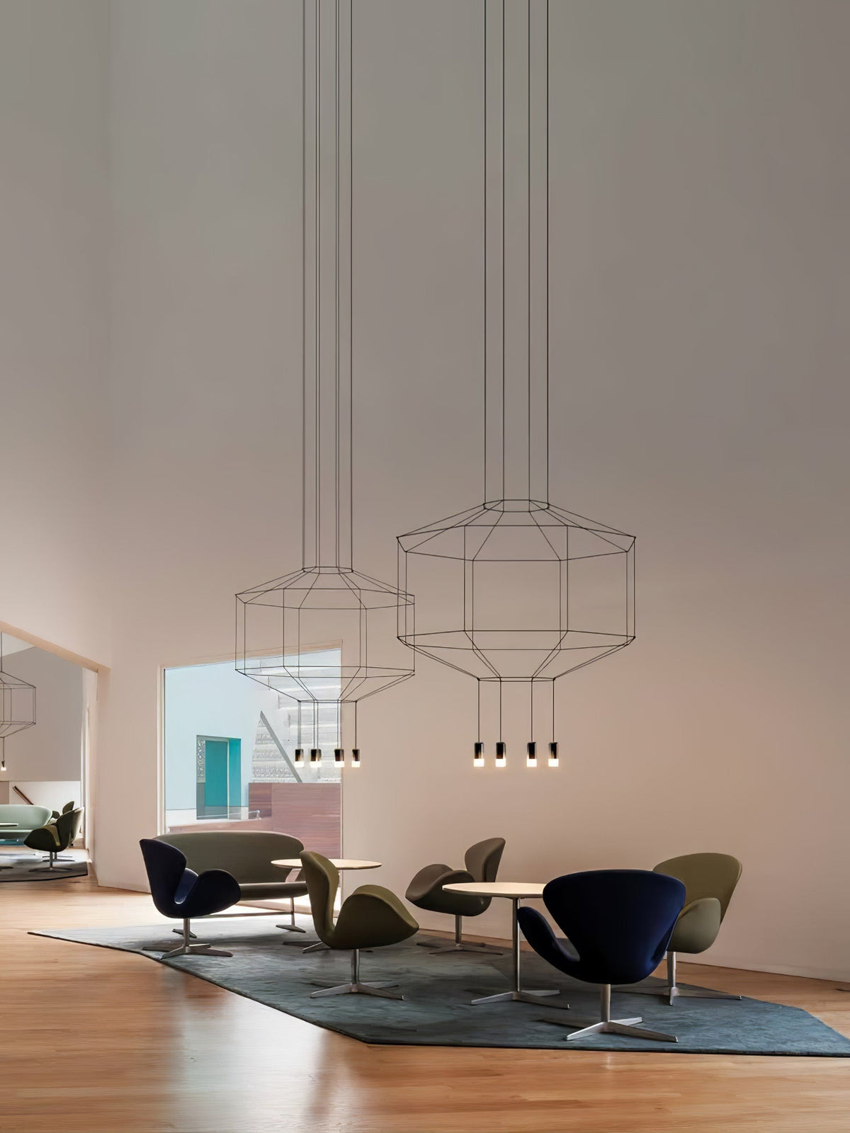 Two Clérachic wireframe pendants hang high in a tall room above a seating group of olive and navy armchairs.