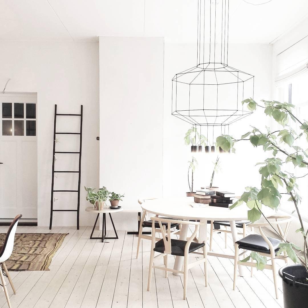 Clérachic wireframe pendant hung over a round white table with Wishbone-style chairs, a ladder and a large green plant behind it.