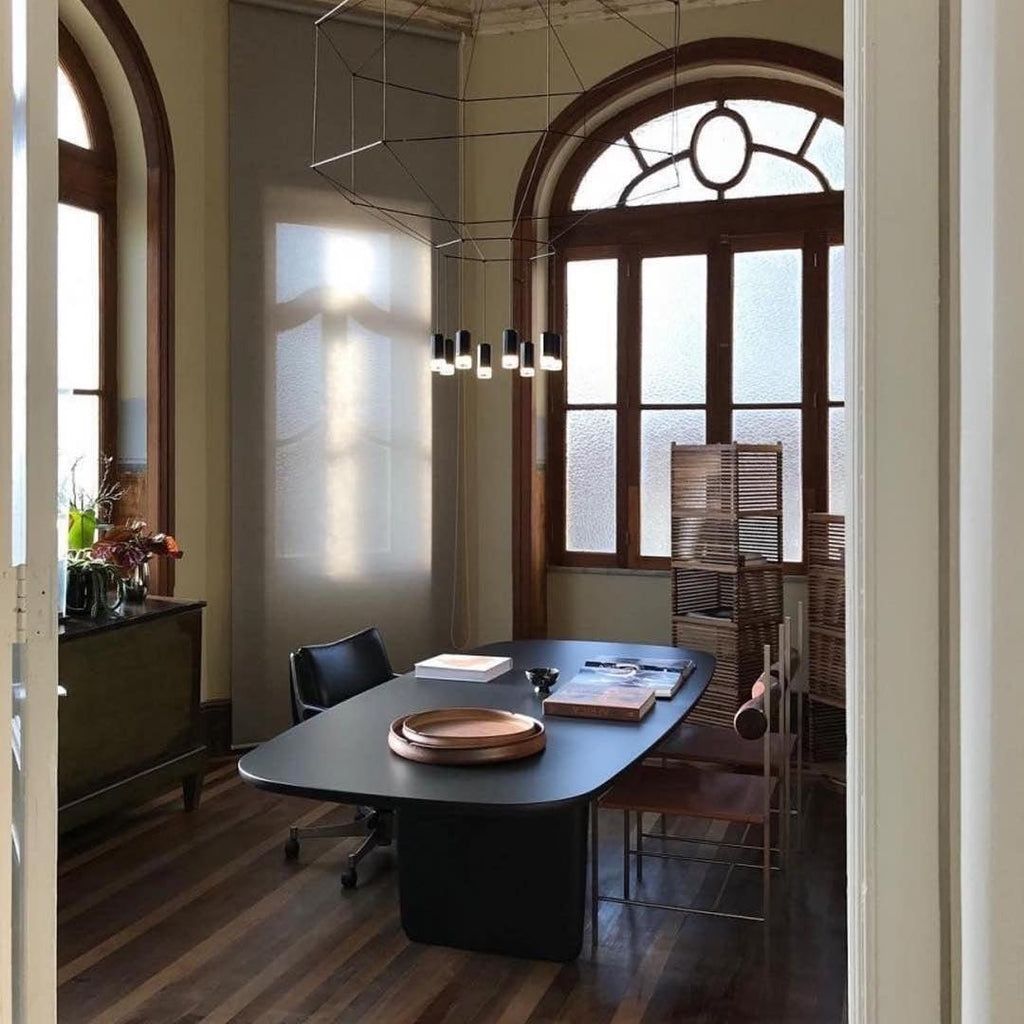 Clérachic wireframe pendant over a dark oval table in a room with tall arched windows and wood floors.