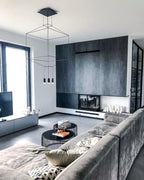 Square-framed black pendant above a grey sofa and round coffee tables in a modern living room, from Clérachic.