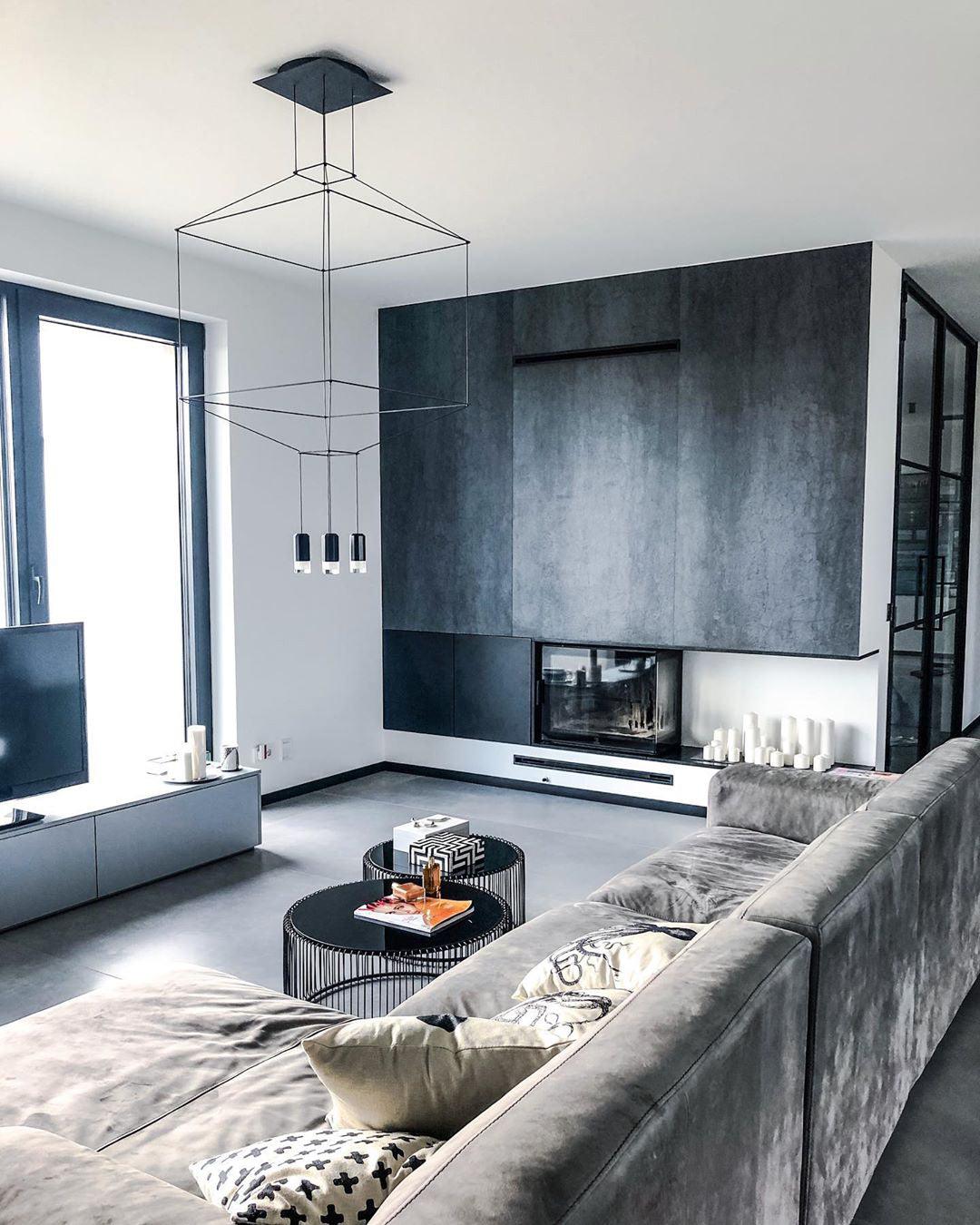 Square-framed black pendant above a grey sofa and round coffee tables in a modern living room, from Clérachic.