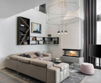 Octagonal cable-frame pendant in a double-height living room with a corner sofa, a fireplace and open shelving, from Clérachic.