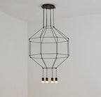 Black wireframe pendant with a canopy, a tiered cage and four lit heads, against a white wall, from Clérachic.
