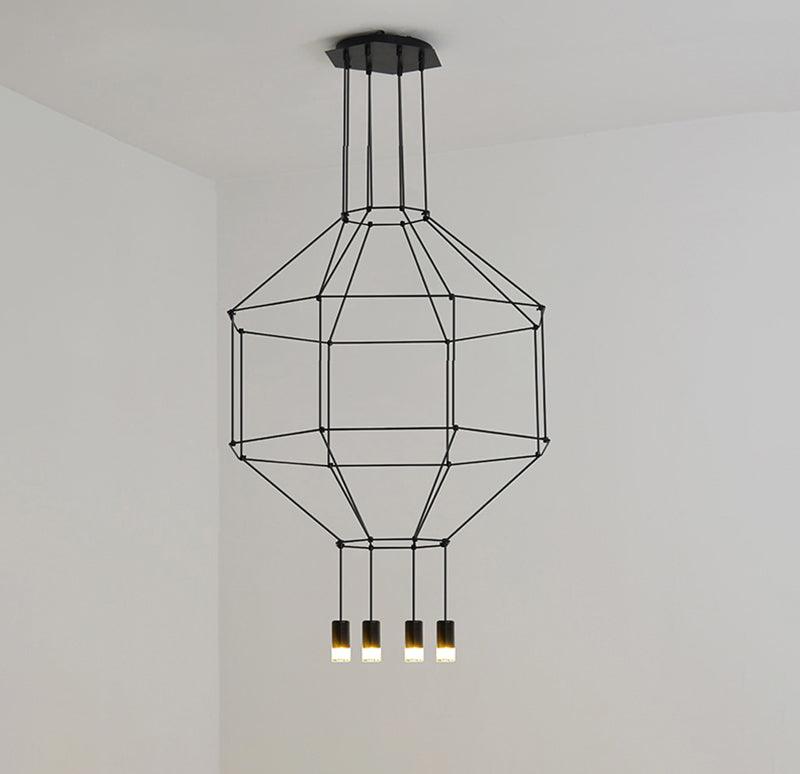 Black wireframe pendant with a canopy, a tiered cage and four lit heads, against a white wall, from Clérachic.