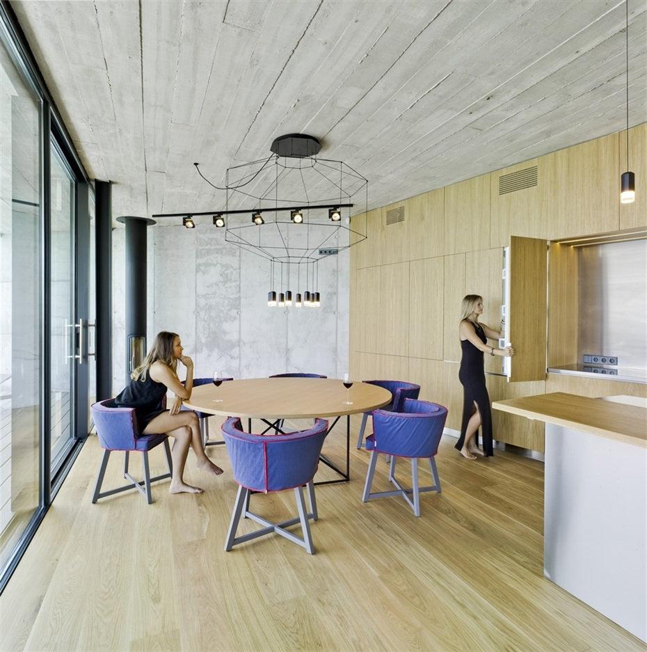 Clérachic wireframe pendant over a round table with purple armchairs, a concrete ceiling and timber panelling.