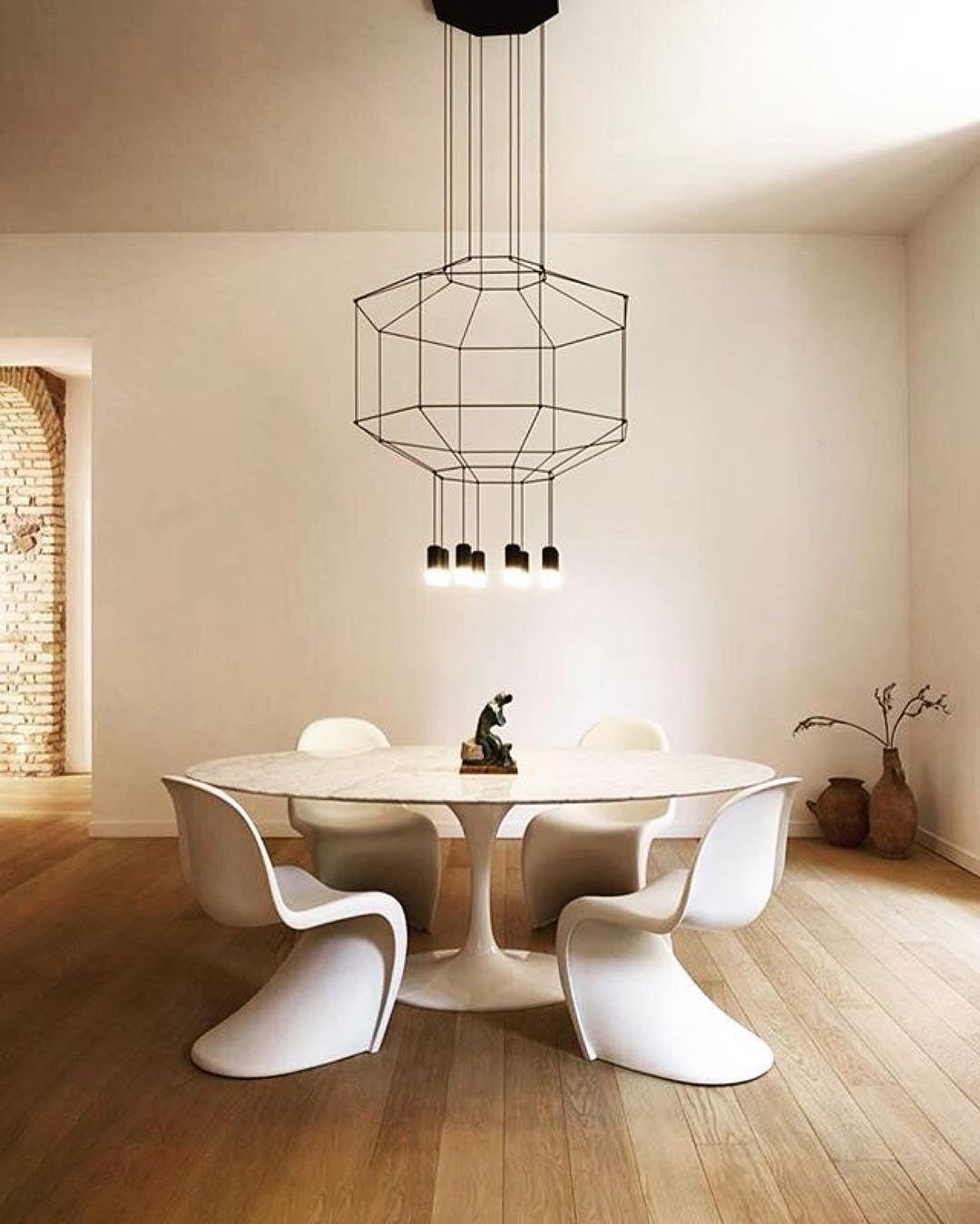 Wireframe pendant above a round white table with moulded chairs in a bare, bright room with a wood floor, from Clérachic.