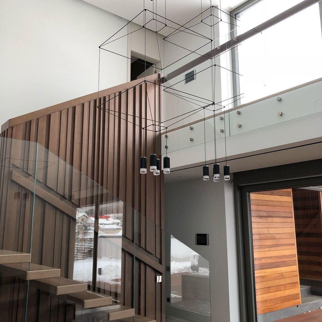 Cube wireframe pendants in a stairwell with a glass balustrade and a timber-clad wall, from Clérachic.
