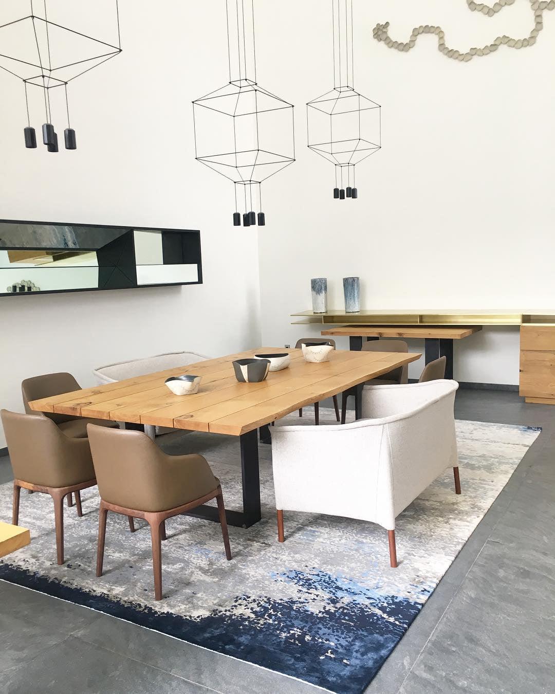 Cube-framed pendants hang above a wooden dining table with tan chairs and a patterned rug, from Clérachic.