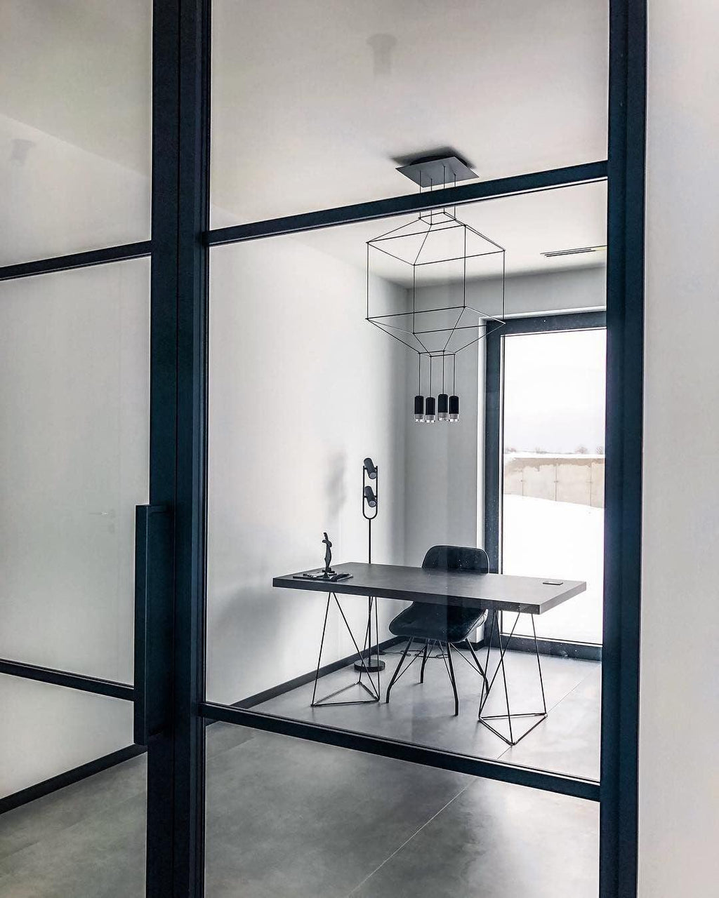 Wireframe pendant in a small office behind a black-framed glass door, with a desk and a chair, from Clérachic.