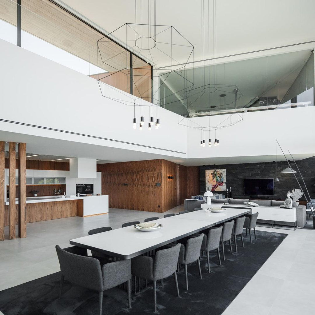 Two wireframe pendants hang in a double-height space above a long white dining table with grey chairs, from Clérachic.