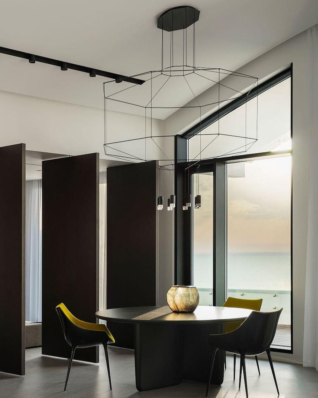 Octagonal wireframe pendant over a round black table with yellow and black chairs and a glass wall, from Clérachic.