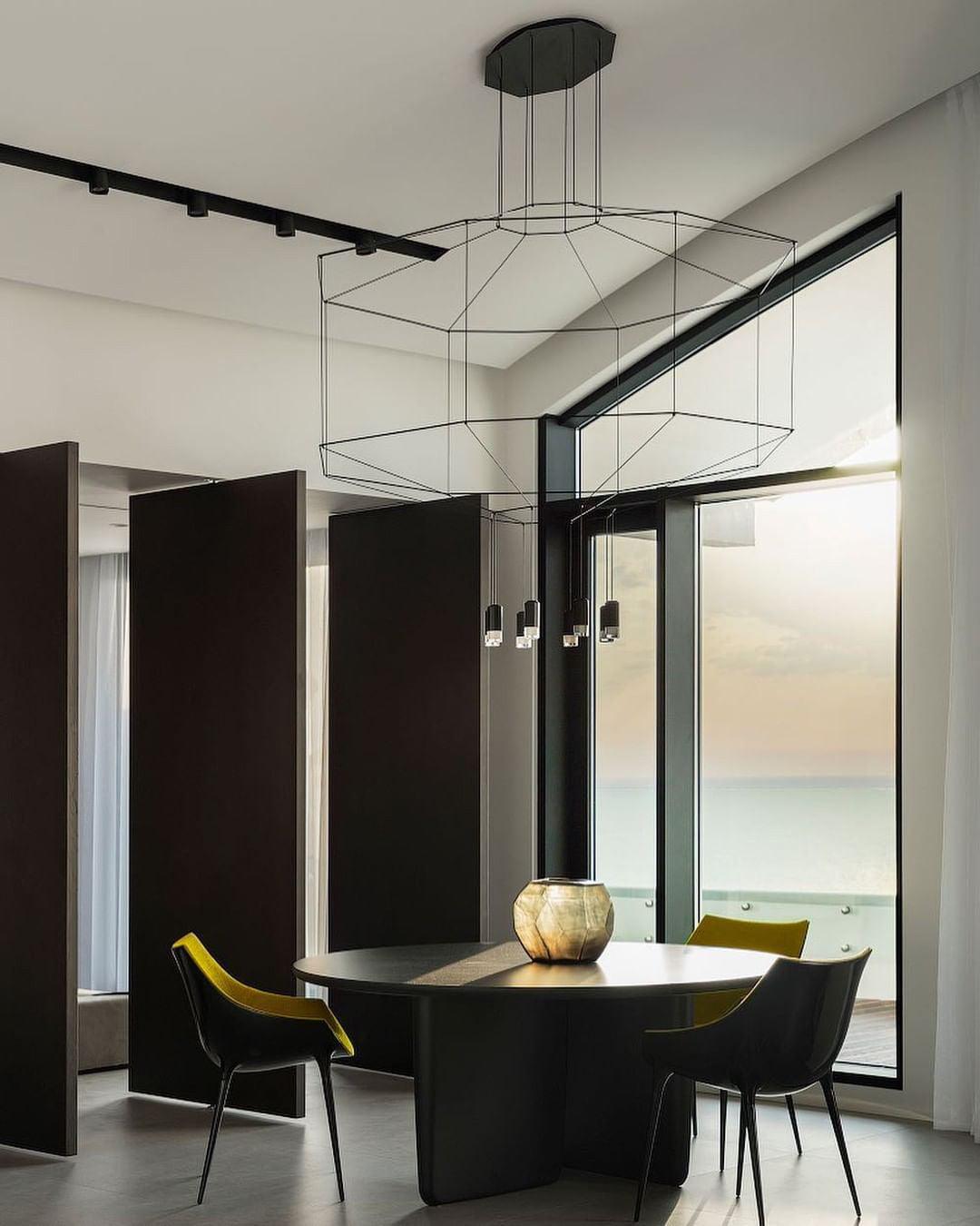 Octagonal wireframe pendant over a round black table with yellow and black chairs and a glass wall, from Clérachic.