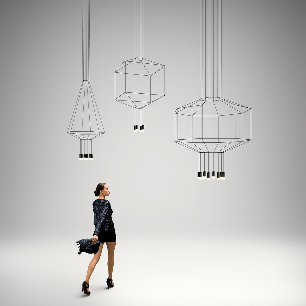 Three Clérachic wireframe pendants in cone, cube and octagon shapes, with a woman in a black dress walking below them.