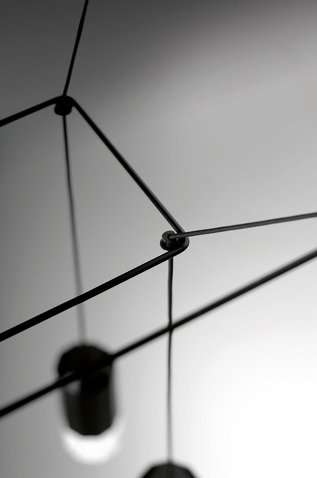Close view of a cable joint with a black light head blurred below, on this Clérachic wireframe pendant.
