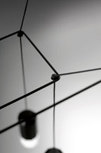 Close view of a cable joint with a black light head blurred below, on this Clérachic wireframe pendant.