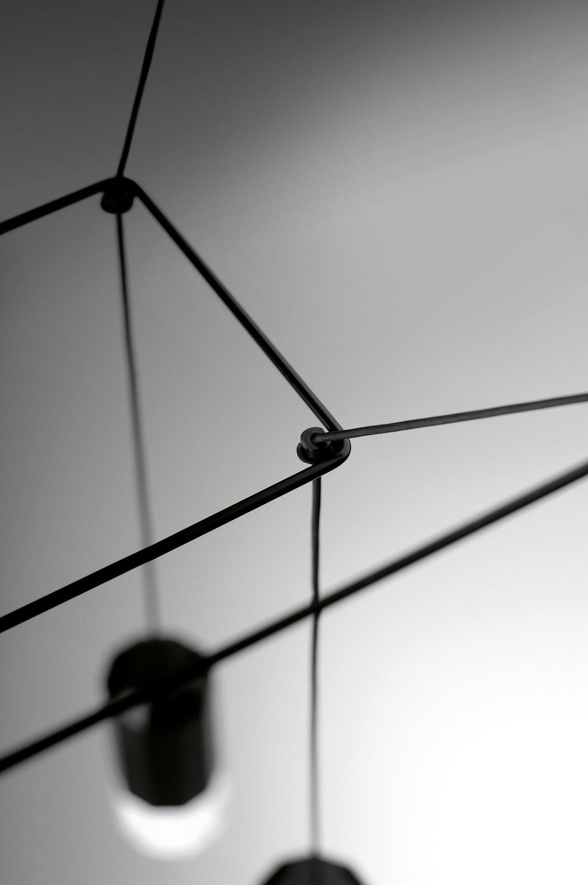 Close view of a cable joint with a black light head blurred below, on this Clérachic wireframe pendant.