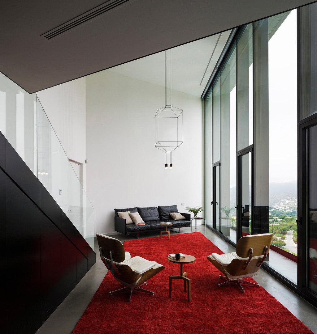 Cube wireframe pendant in a tall room with glass walls, a red rug and two lounge chairs, from Clérachic.