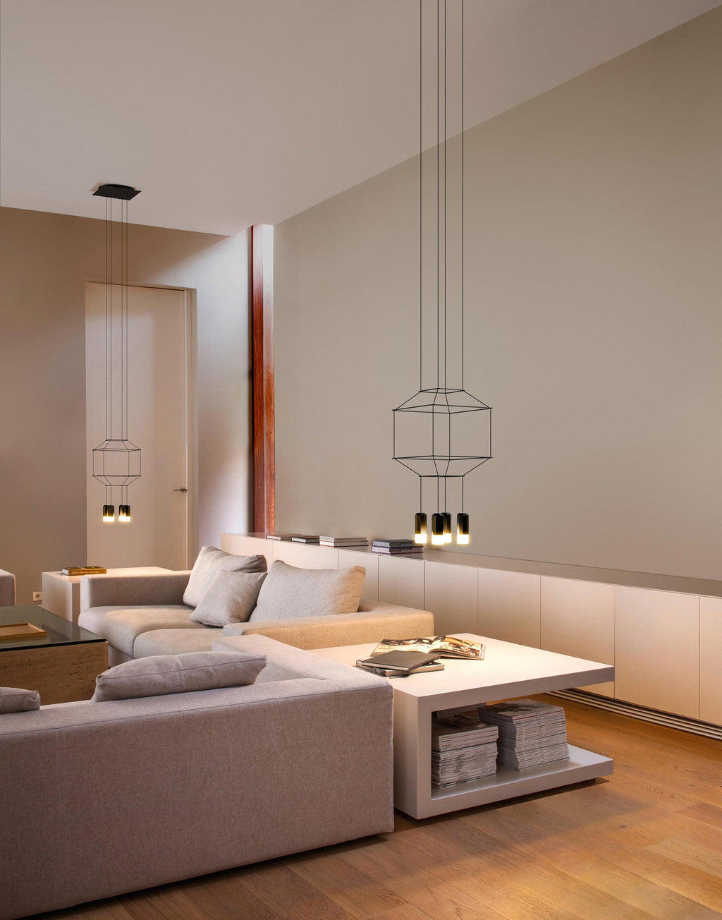 Two wireframe pendants of different sizes above a cream sofa and a low table in a loft living room, from Clérachic.