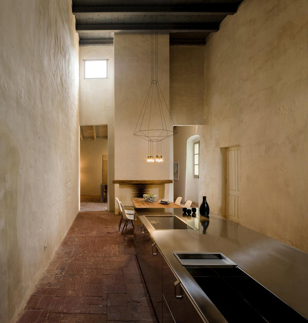 Cone-shaped wireframe pendant at the end of a long kitchen with plaster walls and a brick floor, from Clérachic.