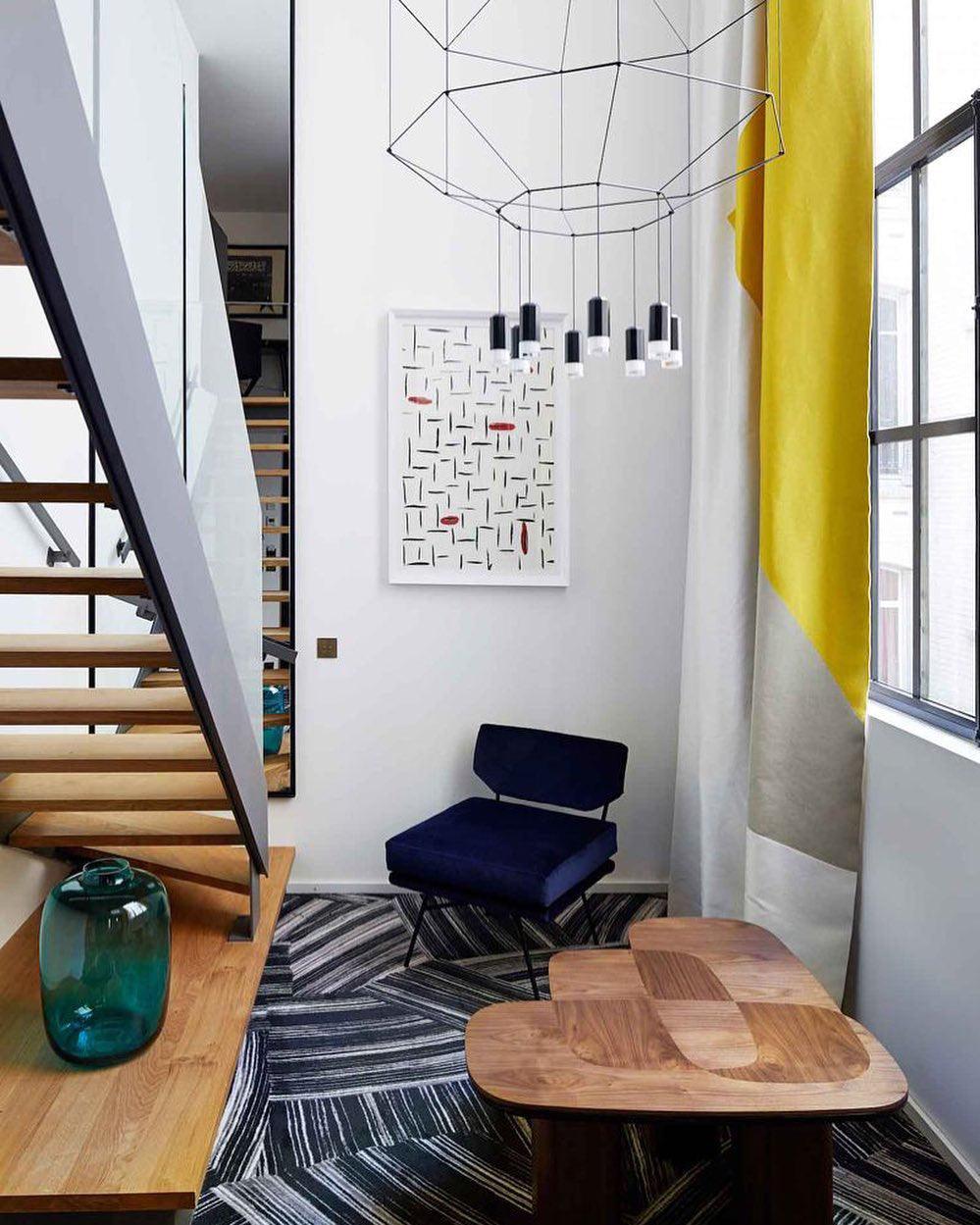 Octagonal wireframe pendant with a cluster of lights above a stair landing with a navy armchair and a wooden table, from Clérachic.