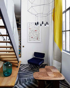 Octagonal wireframe pendant with a cluster of lights above a stair landing with a navy armchair and a wooden table, from Clérachic.