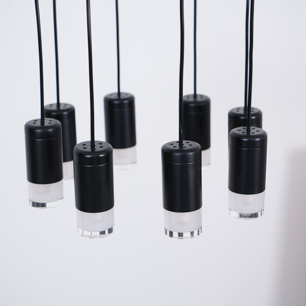 Close view of black cylindrical light heads with perforated tops and frosted bases, hanging on black cables, from Clérachic.