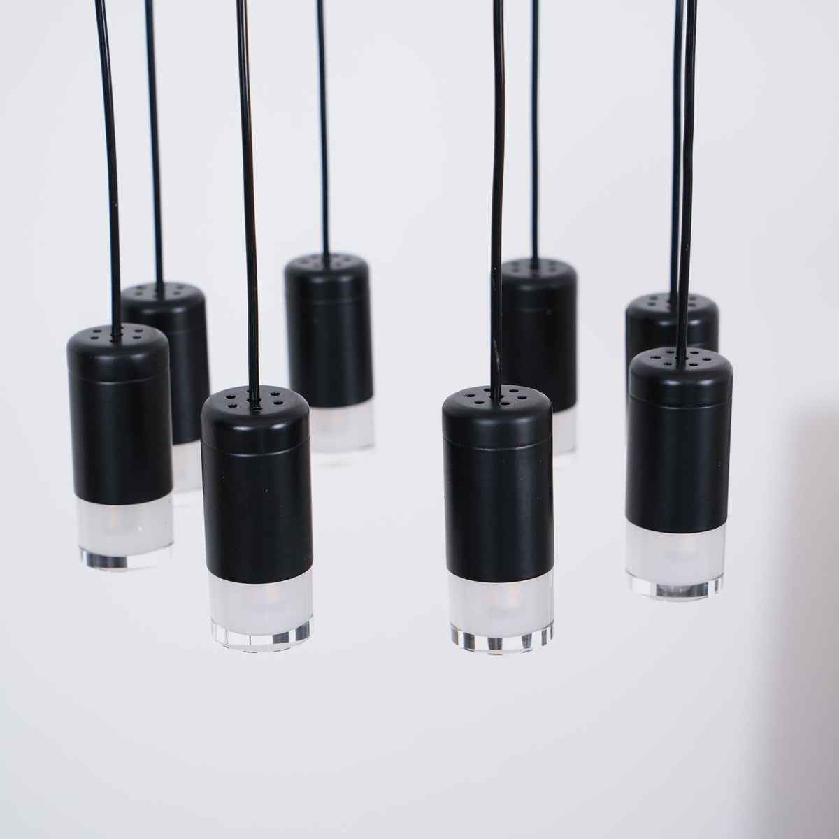 Close view of black cylindrical light heads with perforated tops and frosted bases, hanging on black cables, from Clérachic.
