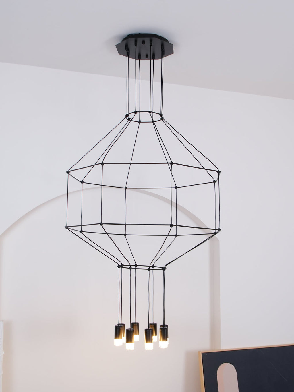Wireframe pendant with its lights switched on, hung on a ceiling canopy before a white wall, from Clérachic.